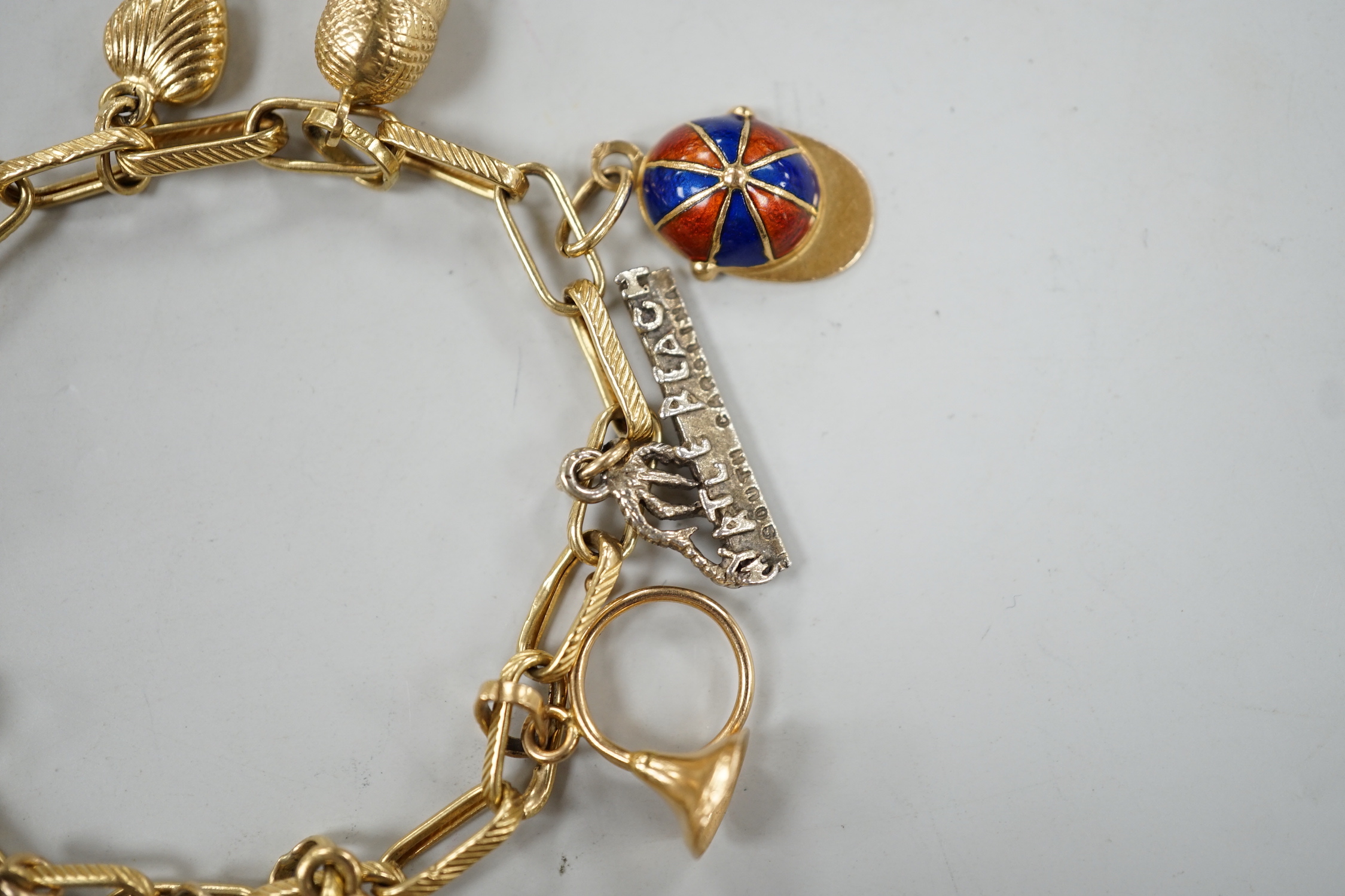 A modern Italian yellow metal charm bracelet, hung with eleven assorted charms, including 750 and enamel jockey cap, agate clasped hand and 750 acorn